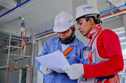 two men in hard hats looking at white paper together