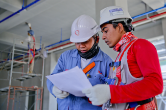 two men in hard hats look at a white paper together